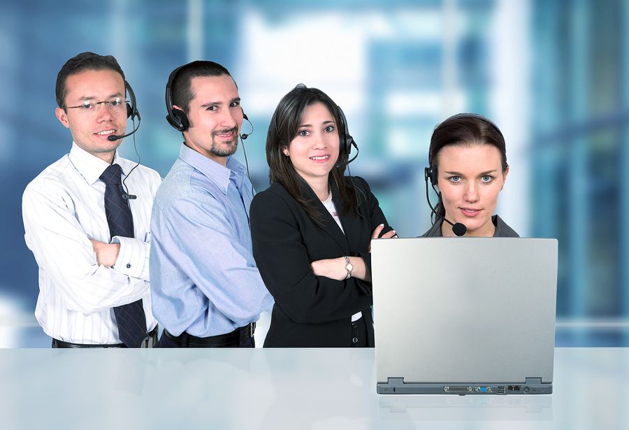 A team of customer support agents wearing headsets, gathered around a laptop