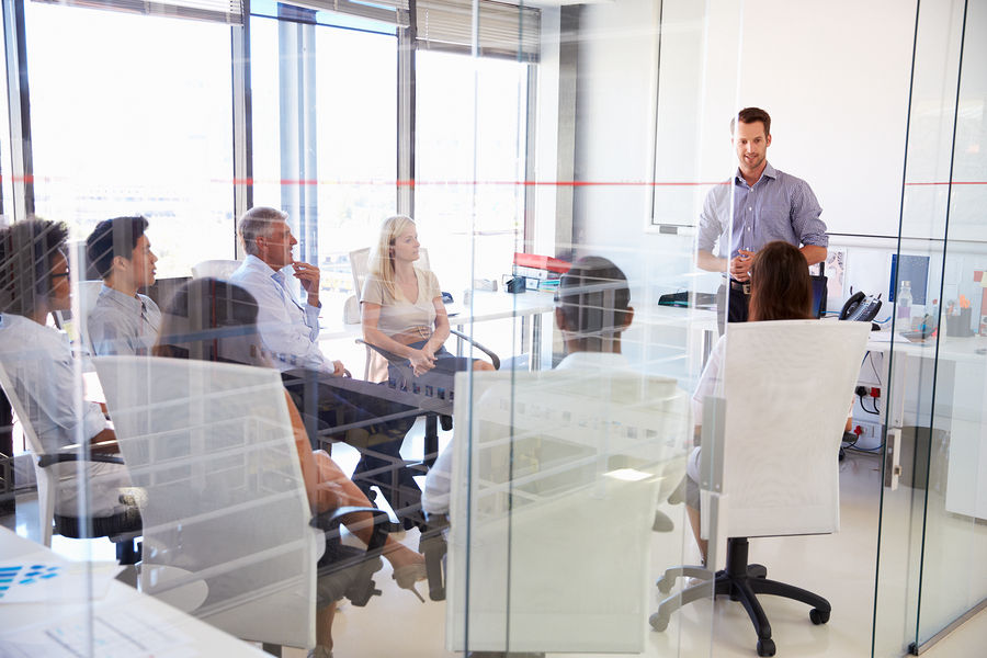 A facilitator presenting to a small group in a modern glass-walled meeting room